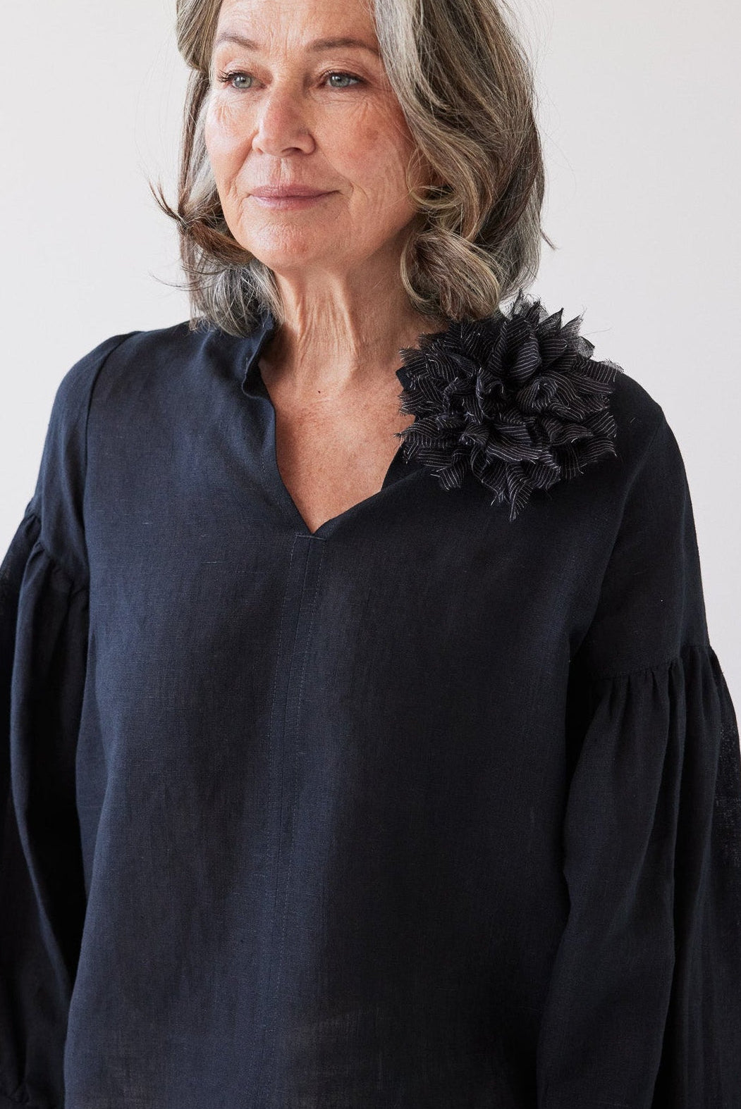 Woman wearing a dark blue blouse with a black floral accessory on a white background