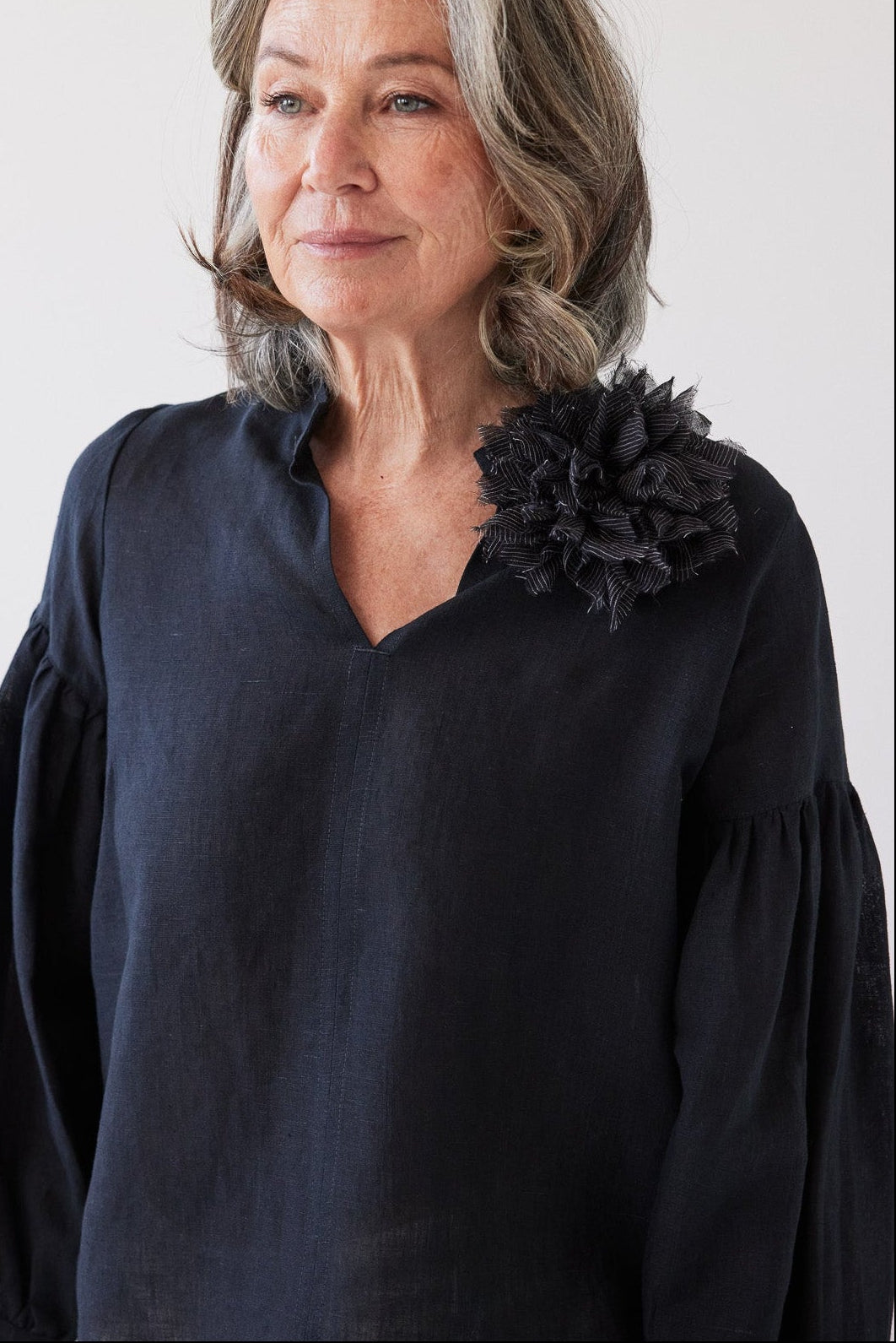 Woman wearing a dark blue blouse with a black floral accessory on a white background